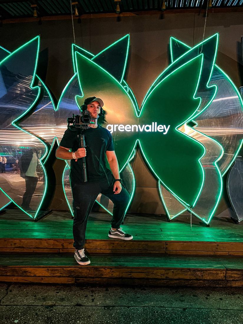 Juan with his camera in front of the Greenvalley sign
